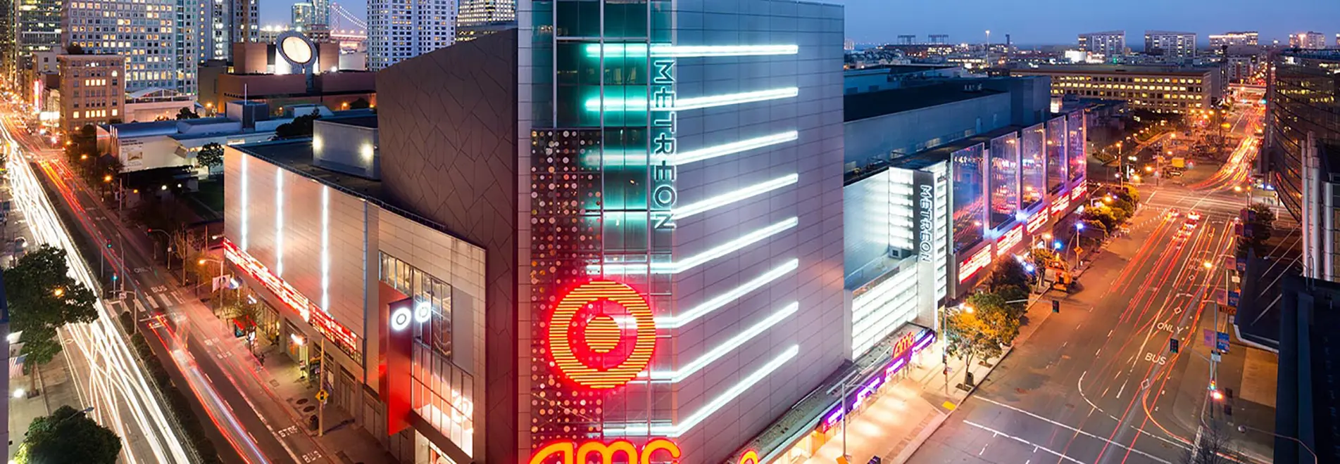 Bird’s Eye View of the Metreon Shopping plaza and AMC storefront there at night, with the San Francisco city skyline and Bay Area real estate in the background
